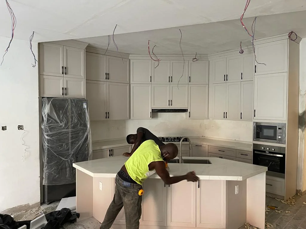 Installer fitting the white cabinet doors on a kitchen island, with wall cabinetry behind